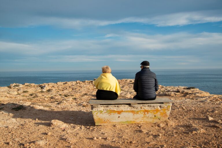 Elderly couple sitting on a bench by the seaside, enjoying a peaceful day.