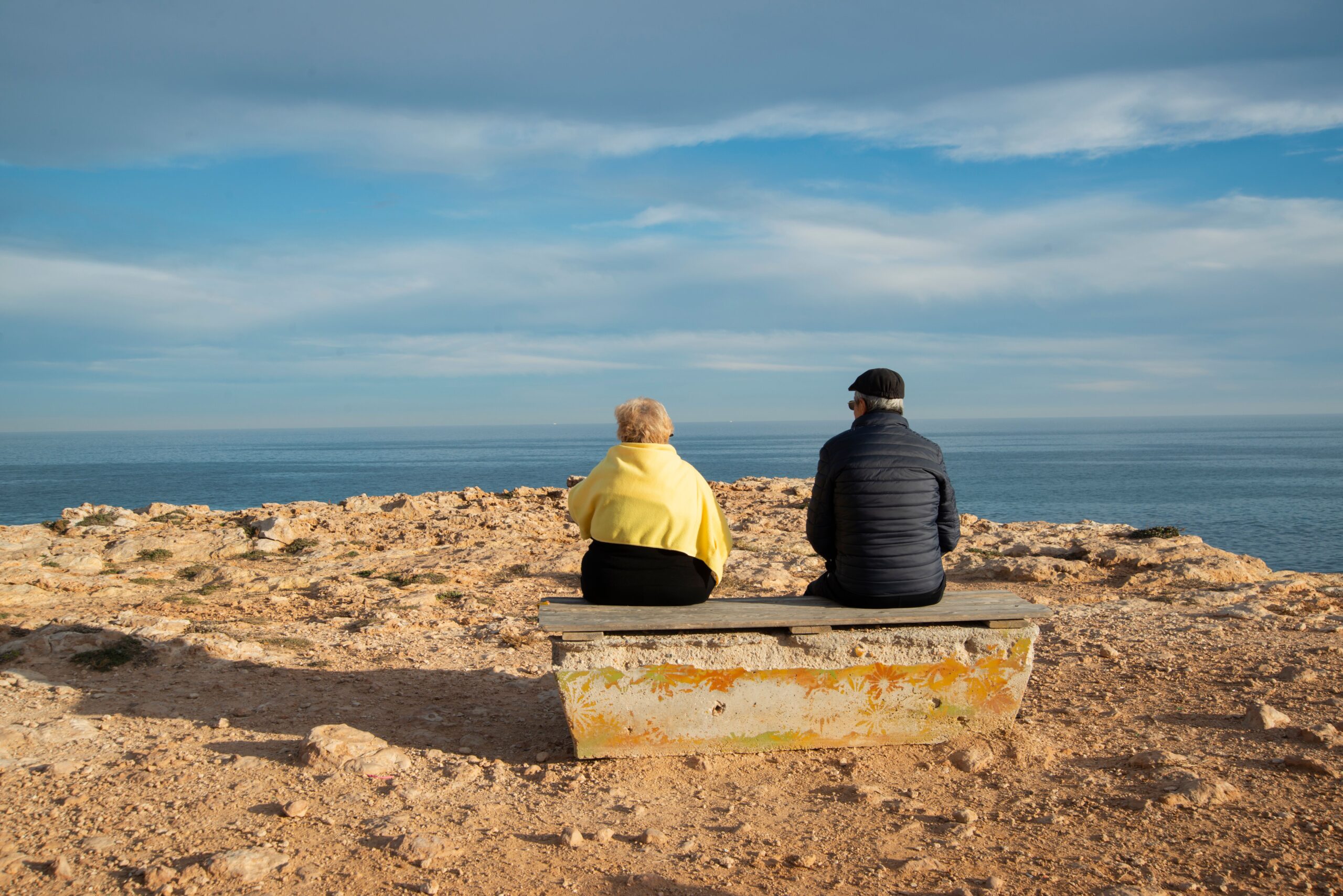 Elderly couple sitting on a bench by the seaside, enjoying a peaceful day.