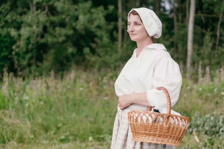 Portrait of a woman in vintage outfit carrying a wicker basket in a lush green field.