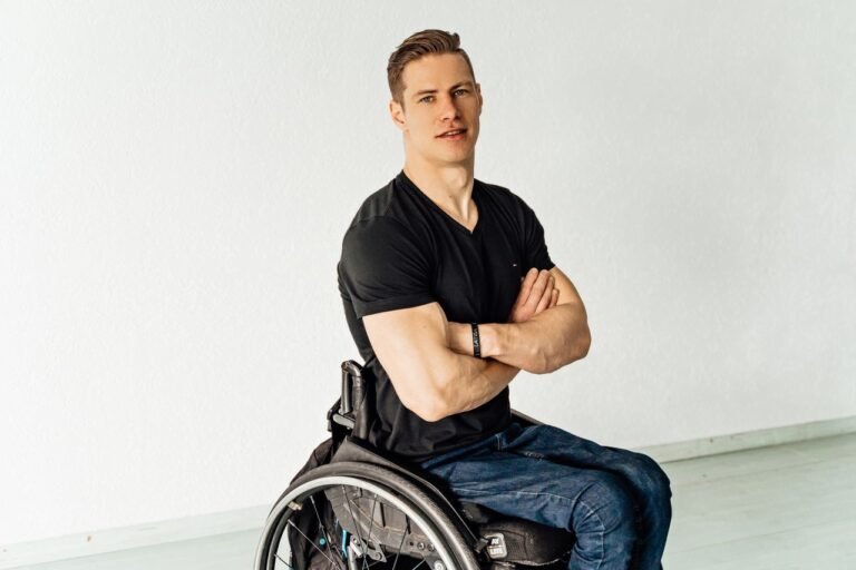 Portrait of a confident young man sitting in a wheelchair indoors with crossed arms.